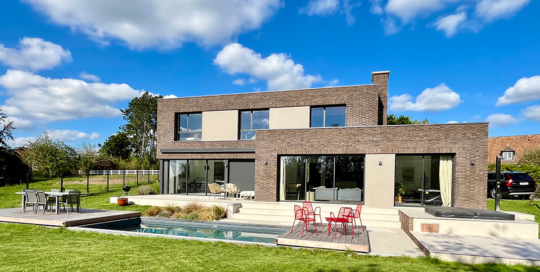 Maison cubique en briques brunes. Façade jardin et piscine.